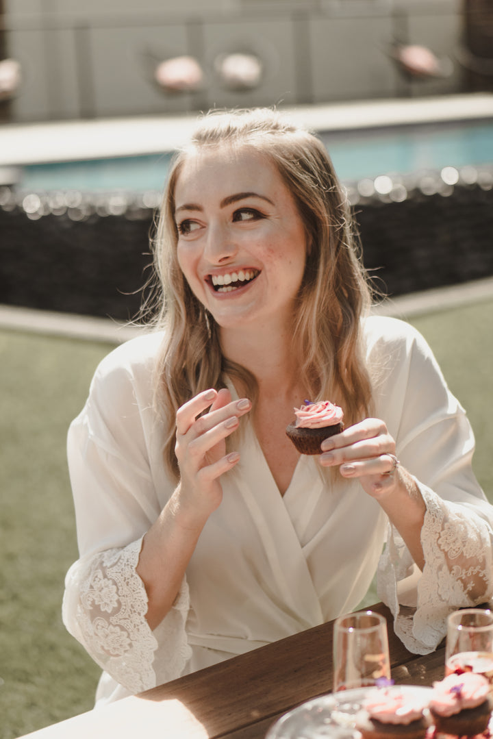 Bride wearing Lily white satin lace bridal robe eating cupcake